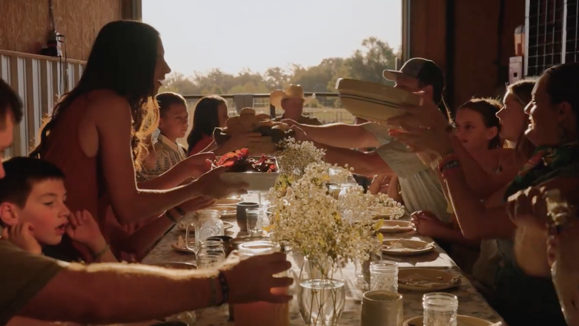 Neighbors sharing a long-table supper in the barn at sunset