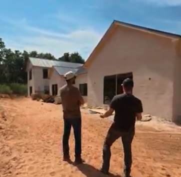 Chase and a partner walking toward a home under construction on a red-dirt lot